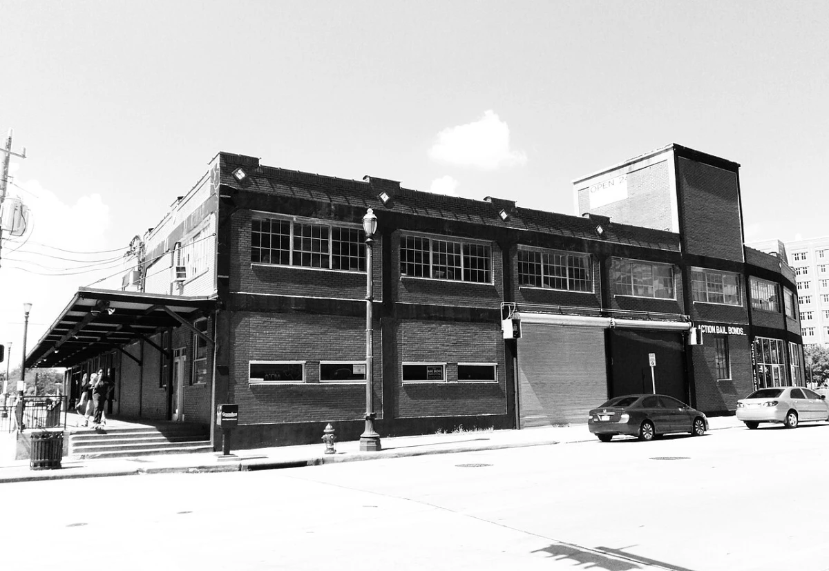 Black and white photo of a long two story brick building at a downtown Houston corner with a bail bonds sign near the far end