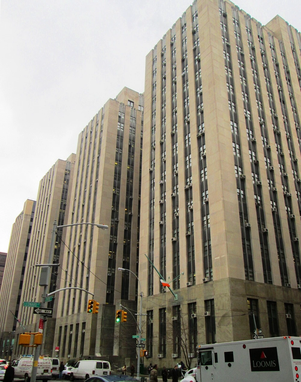 The tall tan stone Criminal Courts Building at 100 Centre Street in Manhattan, seen from the street with traffic lights and vans in front
