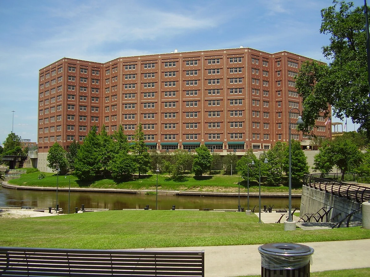 A tall red brick jail building run by the Harris County Sheriff's Office, seen across a park and a bayou in Houston, Texas